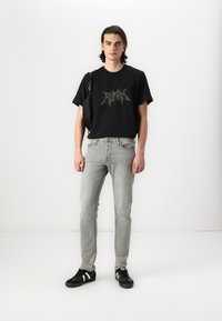 Svart grafisk t-skjorte med sølvlogo, lysegrå smale jeans og svarte sneakers med hvite detaljer. Enkel skulderveske på venstre skulder.