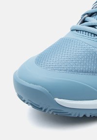 Chaussure de sport bleu clair avec une tige en mesh texturé, un bout en caoutchouc lisse et une semelle blanche contrastante. Caractérisée par un design à lacets et une forme arrondie.