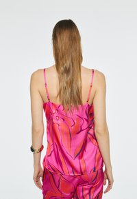 Camisola di satin fucsia con spalline sottili, caratterizzata da un motivo floreale tropicale in arancione e blu navy. Tessuto liscio e vestibilità ampia.