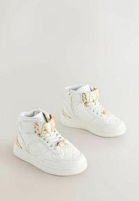 Hvide høj-top sneakers med tekstureret materiale, guld hardware accenter og et distinkt "BAKE" bånd henover fronten. Glat gummisål.