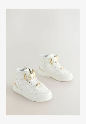 Valged kõrged spordijalatsid tekstuurse materjali, kuldsete detailide ja erilise "BAKE" rihmaga ees. Sile kummist tall.