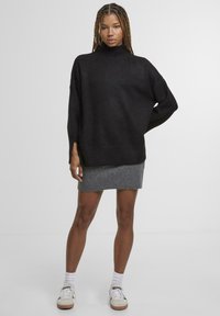 Sort oversized sweater med høj hals, parret med en grå nederdel. Outfittet inkluderer hvide strømper og sneakers, hvilket viser en afslappet pasform.