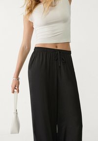 Černé kalhoty s širokými nohavicemi, elastickým pasem a šňůrkou. V kombinaci s bílým těsným crop topem a malou bílou kabelkou.