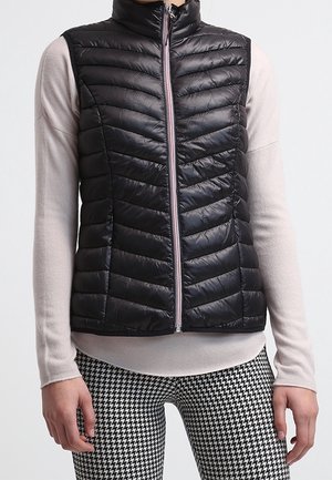 Sleeveless black quilted puffer vest with front zipper worn over a light beige long-sleeve top and black-and-white houndstooth pants.