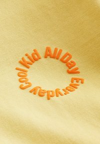 Gelbes Material mit einem orangen, kreisförmigen, gestickten Textdesign, das "Cool Kid All Day Everyday" sagt. Glatte Textur, lässiger Stil.