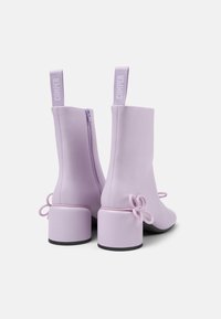 Stivaletti alla caviglia lilla in materiale liscio, con chiusura a zip, tacco spesso e fiocchi decorativi sui lati.