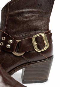Bota de tobillo de cuero marrón con detalle de hebilla dorada, tacón robusto y acentos de costura, con una textura suave y un diseño de punta redonda.