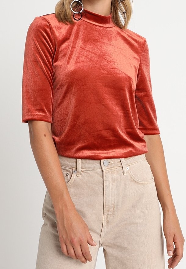 Haut en velours de couleur rouille avec un col montant et des manches courtes, associé à un jean taille haute beige clair. Texture lisse et coupe ajustée.