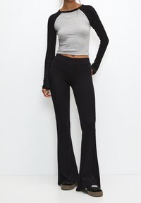 Haut à manches longues gris et noir, coupe ajustée, associé à un pantalon évasé noir côtelé. Les deux présentent une texture lisse et des accents simples.