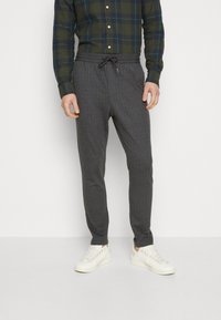 Grå mønstrede joggingbukser med snøre i taljen, lavet af blødt stof, parret med hvide sneakers og en grønternet skjorte.
