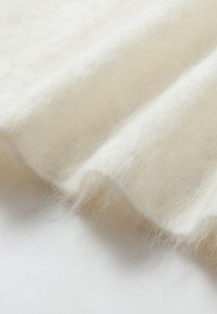 Tessuto in feltro bianco con una consistenza morbida e soffice, caratterizzato da delicate ondulazioni. Il materiale appare leggero e caldo, ideale per abbigliamento o accessori.