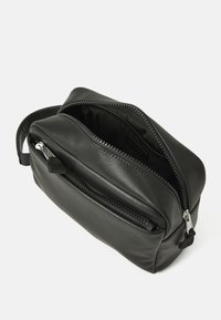 Borsa nera in pelle con una superficie liscia, forma rettangolare, doppie tasche con zip e una maniglia laterale per il trasporto.