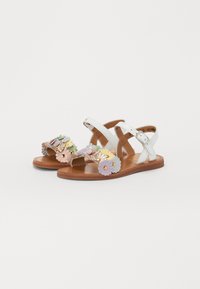 Sandales en cuir blanc avec une semelle marron, ornées d'accents floraux colorés en rose, bleu et jaune, munies de sangles ajustables et d'un design ouvert.