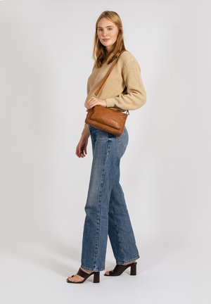 Tan læder crossbody taske med glat overflade, rektangulær form og justerbar rem. Båret sammen med en beige sweater og blå jeans.