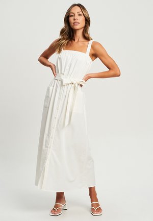 White maxi dress with adjustable straps, a square neckline, button-down front, side pockets, and a tied waist belt. Smooth cotton fabric.
