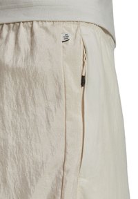 Beige shorts with a textured, shiny fabric, featuring an elastic waistband and a visible zipper pocket with a fabric tag reading "END PLASTIC WASTE."