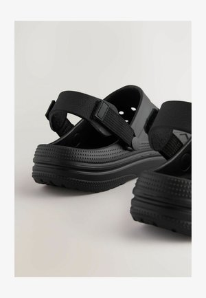 Sandali neri in gomma con cinturini testurizzati, chiusura regolabile con velcro, design perforato e suola imbottita.