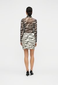 Μακρυμάνικο τοπ με ρίγες ζέβρας σε μαύρο και μπεζ χρώμα σε συνδυασμό με μίνι φούστα με το ίδιο μοτίβο ζέβρας· η μοντέλο φοράει μαύρα παπούτσια με τακούνι.