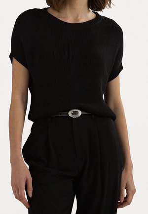 Žena nosící černý žebrovaný pletený top s krátkým rukávem zastrčený do černých kalhot s vysokým pasem a stříbrnou sponou na pásku.