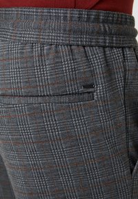 Szare spodnie w kratę z delikatnym wzorem w houndstooth, z dopasowanym pasem i tylną kieszenią ozdobioną poziomym przeszyciem.