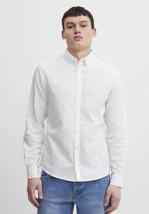 White long-sleeve button-up shirt in lightweight fabric, featuring a classic collar and yellow buttons, paired with blue denim jeans.