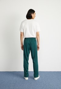 Zelene športne hlače z elastičnim pasom in belimi stranskimi črtami, kombinirane z enostavno belo majico. Gladka tekstura, sproščen kroj.