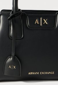 Borsa a mano in pelle nera con accessori in oro. Presenta il logo "A|X" in rilievo e la scritta "ARMANI EXCHANGE". Texture liscia con design strutturato.