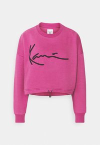 Sudadera corta rosa con logo firmado en negro, escote redondo y mangas largas. Cuenta con cordón ajustable en el dobladillo. Textura suave.