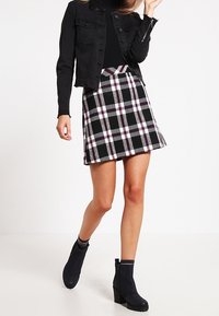 Chaqueta de mezclilla negra sobre una blusa negra ajustada, combinada con una mini falda a cuadros en negro, blanco y púrpura. Botas negras hasta el tobillo con un tacón grueso.