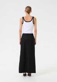 Fustă maxi neagră dintr-un material moale, cu un design simplu, cusătură la talie și slituri laterale. Purtați cu un top alb fără mâneci.