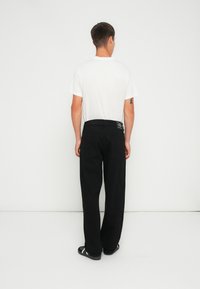 Pantaloni negri cu o croială lejeră, din denim, cu două buzunare la spate și un eticheta la talie. Purtați cu un tricou alb.