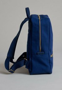 Zaino blu navy realizzato in tela; presenta una cerniera dorata, spallacci regolabili e una tasca anteriore con un design verticale elegante.