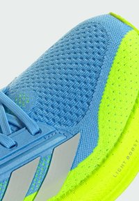 Zapatilla deportiva de color azul claro con una textura de malla, acentos verdes brillantes, detalles plateados y una suela acolchada etiquetada como "LIGHT BOOST".