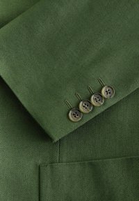 Green fabric sleeve with four sewn translucent brown buttons and visible stitching on a tailored garment.