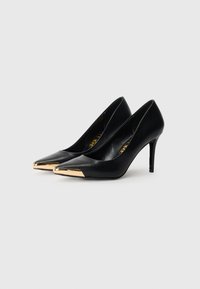 Juodi aukštakulniai bateliai su smailiu nosiu, turintys auksinį metalinį apvalkalą ant nosies ir ploną stiletto kulną. Lygus odos paviršius.