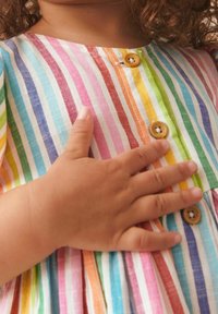 Bunt gestreiftes Kleid aus leichtem Stoff. Mit Holzknöpfen und kurzen Ärmeln. Hand ruht auf der Brust.