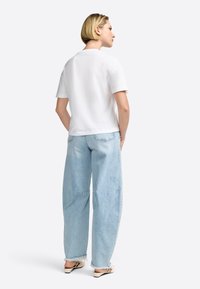 White short-sleeve t-shirt paired with light blue oversized denim jeans, featuring a relaxed fit and frayed hem. Minimalistic design.