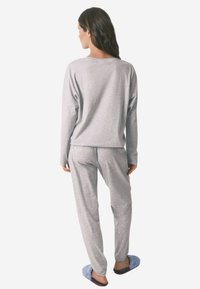 Szary longsleeve i pasujące spodnie piżamowe w nakrapianym wzorze. Strój jest casualowy i wygodny, zestawiony z niebieskimi klapkami.