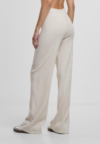 Pantalons larges beige avec une taille haute, en tissu doux et texturé. Présente une coupe décontractée et droite, s'étendant jusqu'au sol.