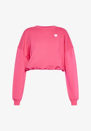 Rožinė trumpa prailginta palaidinė su ilgomis rankovėmis, gumbuotais rankogaliais ir mažuoju baltu širdelės dizainu ant krūtinės. Pagaminta iš minkštos, lengvos medžiagos.