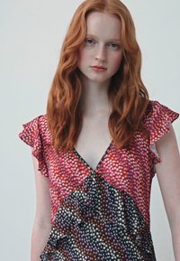 Vestido multicolorido com decote em V, mangas curtas com babados e design em camadas; apresenta um padrão de pontos em tamanhos e cores variados.