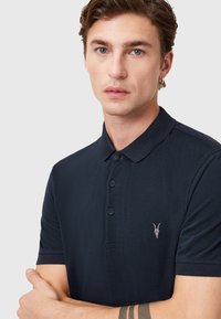 Navy Polo-Shirt aus strukturiertem Stoff, mit Knopfleiste, kurzen Ärmeln und einem kleinen Logoakzent auf der Brust.