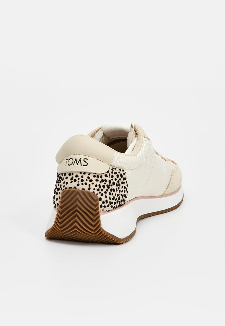 Zapatilla TOMS beige con talón de estampado de leopardo, media suela blanca y suela texturizada marrón, vista desde la parte trasera derecha.
