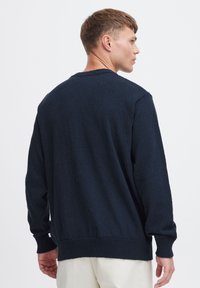 Maglione blu navy con superficie testurizzata, scollatura rotonda e polsini a coste. Presenta una vestibilità rilassata con maniche lunghe e orlo dritto.