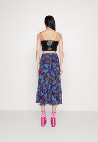 Czarny crop top z cekinami na cienkich ramiączkach, w połączeniu z niebieską spódnicą zdobioną kolorowymi wzorami liści. Różowe sandały na grubym obcasie dopełniają look.