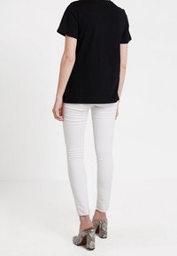 Black short-sleeve top, white fitted jeans, and snake-print high-heeled shoes, viewed from the back. Simple, casual design.