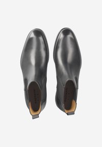 Schwarze Chelsea-Stiefel aus Leder mit glatter Textur, elastischen Seitenteilen und einer Schlaufe zum einfachen An- und Ausziehen. Braunes Innenfutter als Detail.