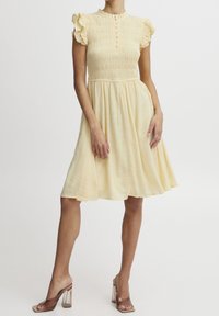 Hellgelbes Kleid mit gerafftem Oberteil, Rüschenshülsen, Knopfverschluss und leicht ausgestellt Rock mit strukturierten Punktmustern.