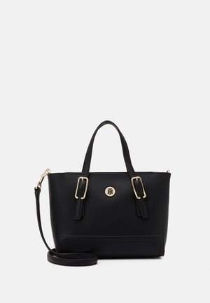 Musta nahkainen käsilaukku, jossa on kaksoiskahvat, säädettävä olkahihna, kullanväriset soljet ja edessä pyöreä kultainen logokuvio.