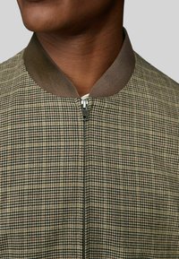 Checkered jacket in beige and brown tones, featuring a smooth finish, ribbed brown collar, and a zippered front closure.